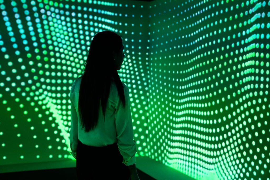 Woman stands before a large LED wall covered in green dots forming waves